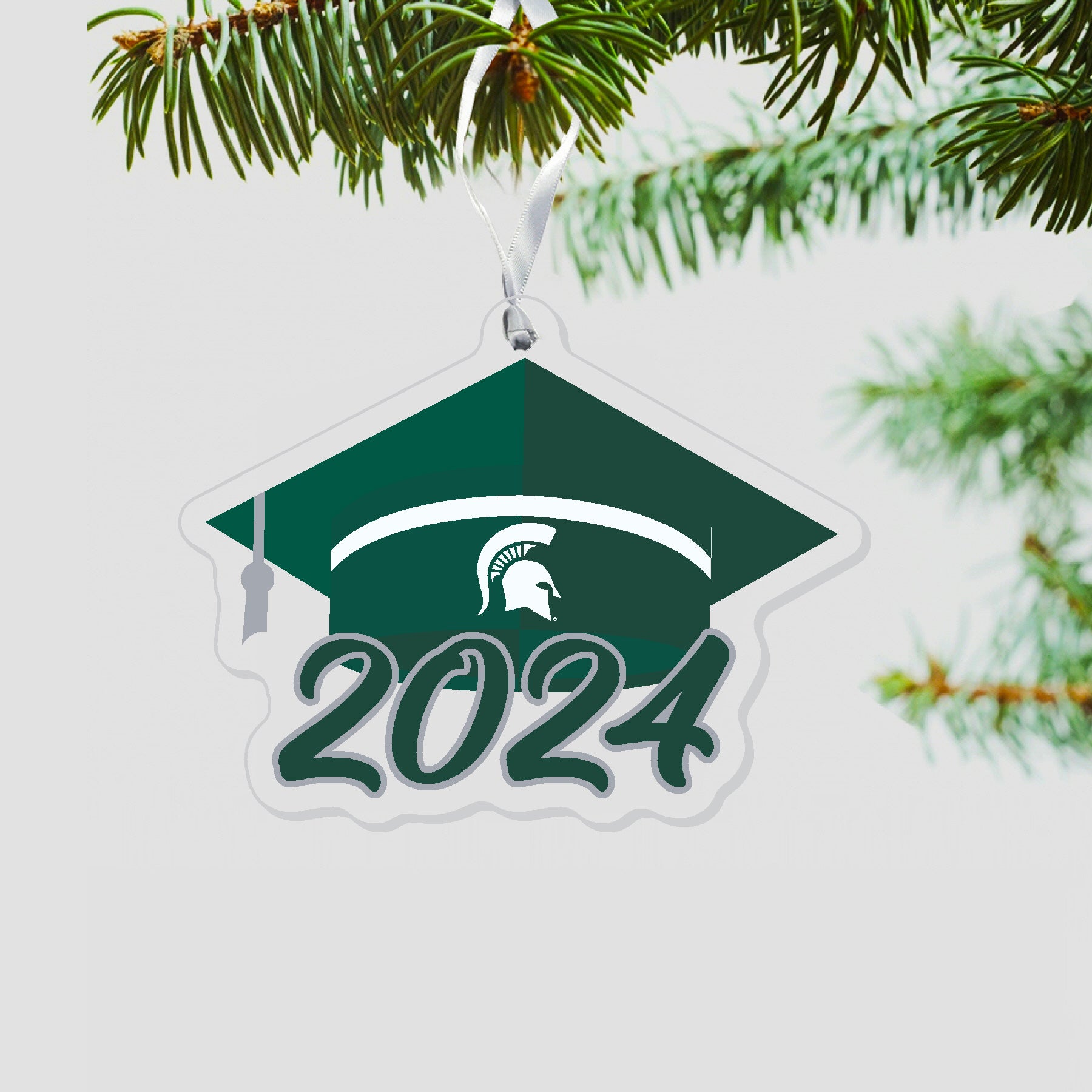 Graduation cap ornament with a white stripe at a base of the cap. White Spartan helmet centered on green band. 2024 is under the cap in green outlined in silver.