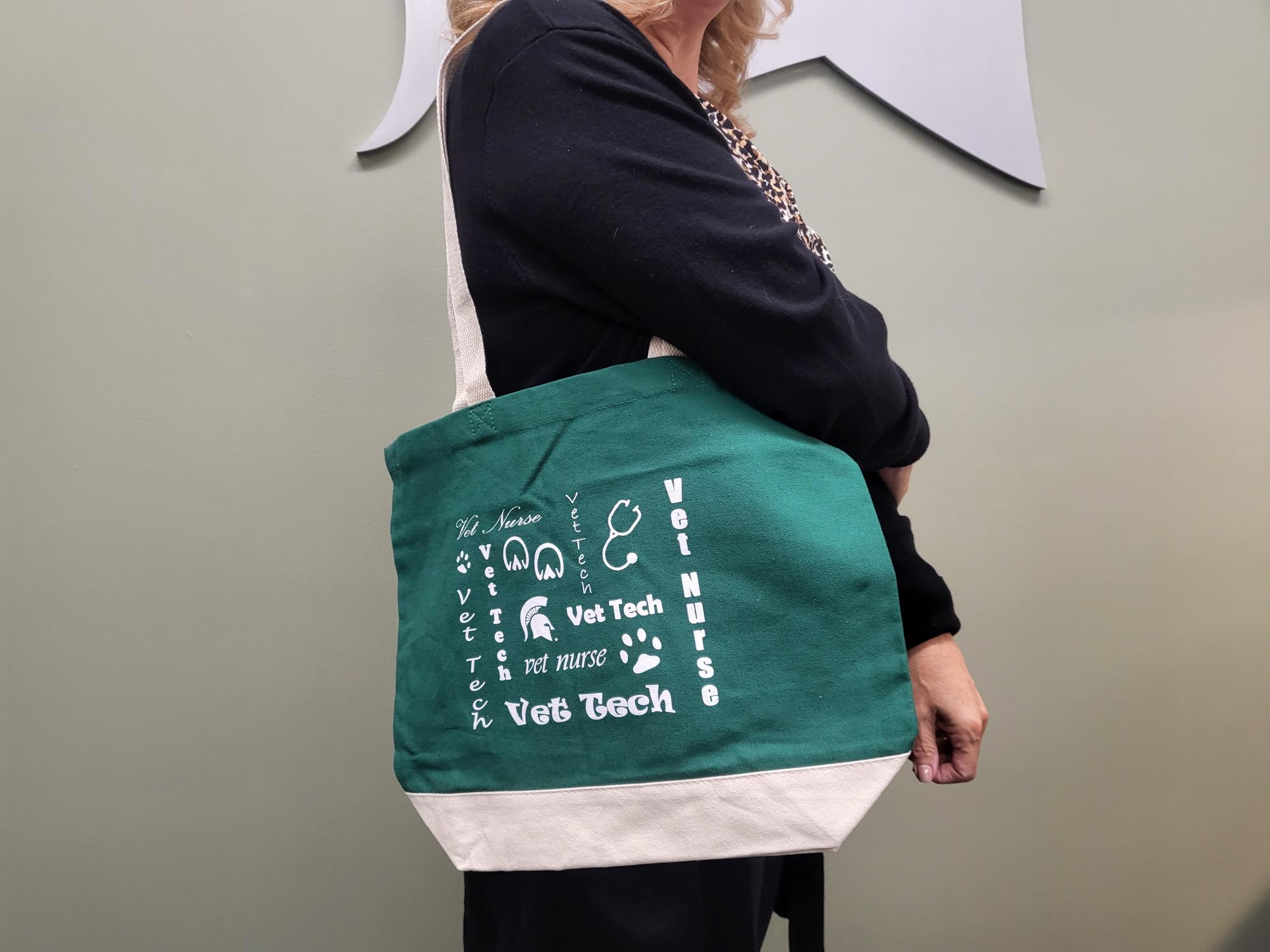 Person with a green canvas tote bag with white straps, a white bottom section, and white 'Vet Tech' text and graphics related to veterinary technology and veterinary nursing.