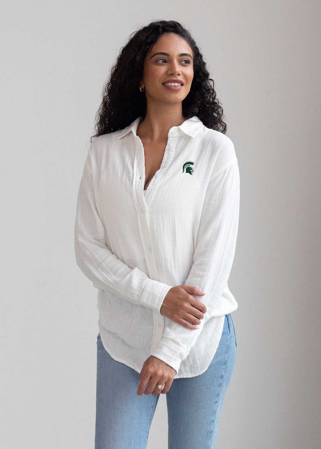 Person in white button-up shirt with green Spartan logo and light blue jeans.