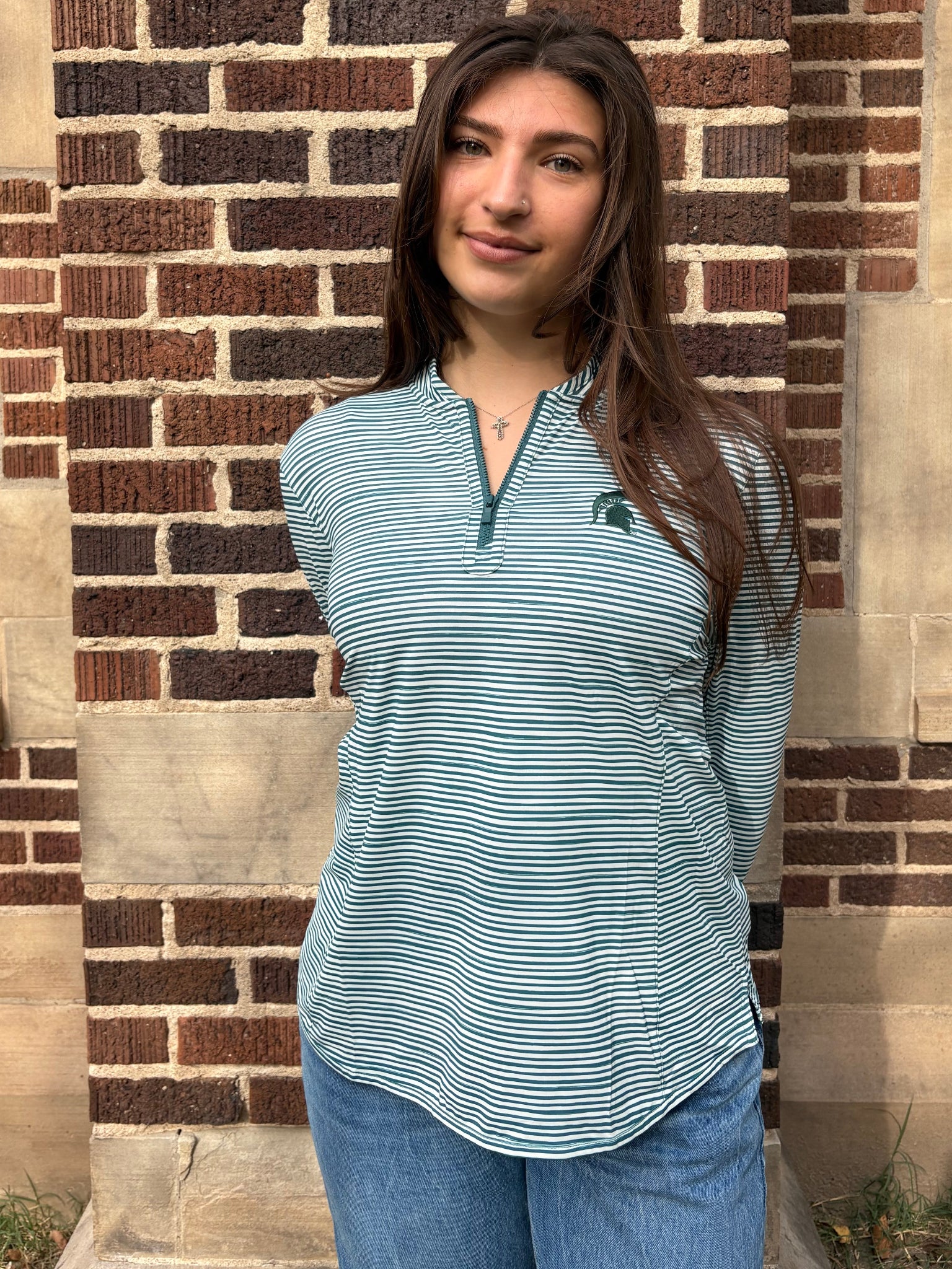 Closer angle of a woman standing outdoors, wearing a green and white striped quarter-zip pullover with a green Spartan helmet logo on the left upper chest.