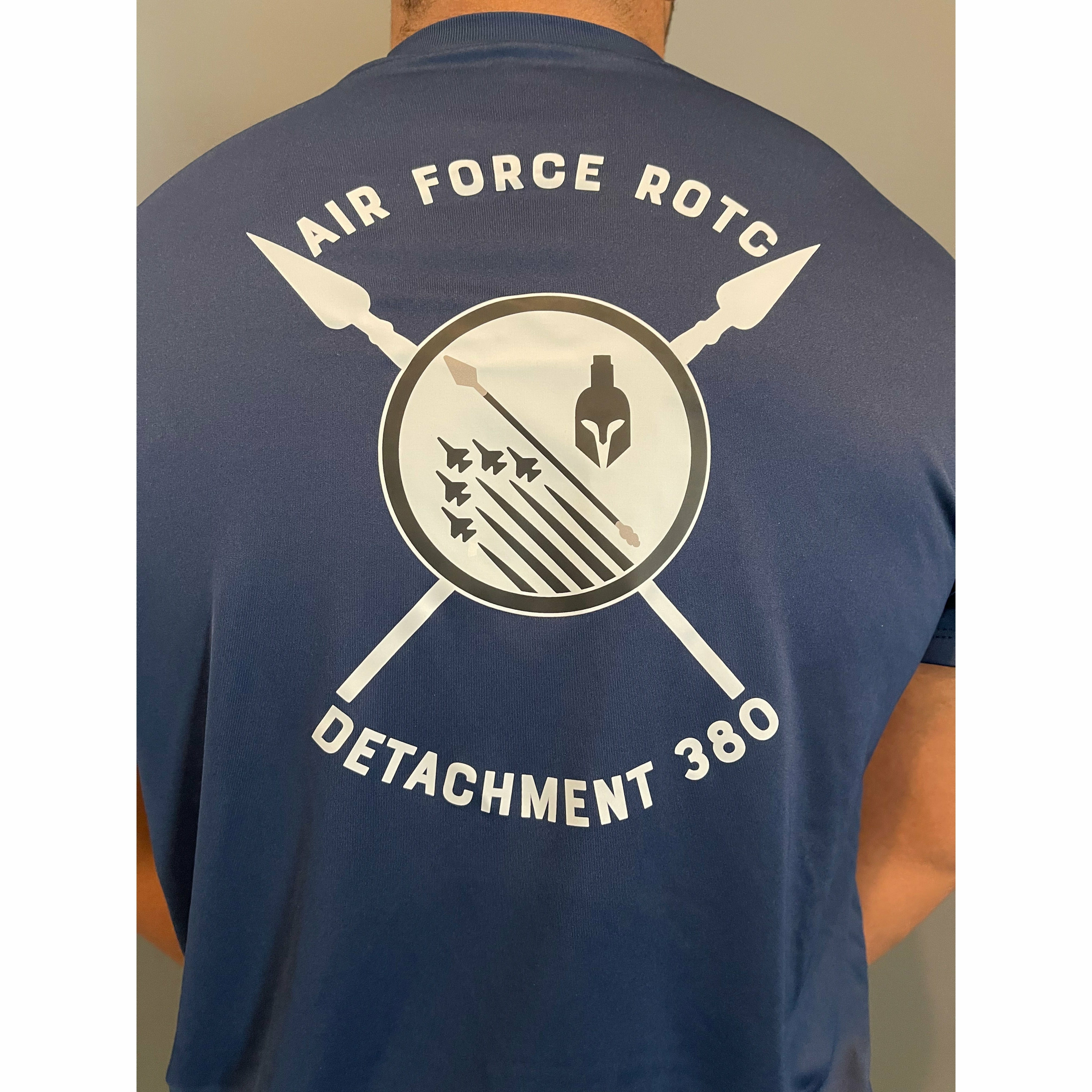 Back of a man wearing a blue athletic t-shirt. On the center is a black and white screen print of the AFROTC detachment 380 logo of 5 fighter jets, a spear, and a spartan helmet over two crossed spears. Along the top and bottom curved text spells out Air Force ROTC Detachment 380 in white block letters