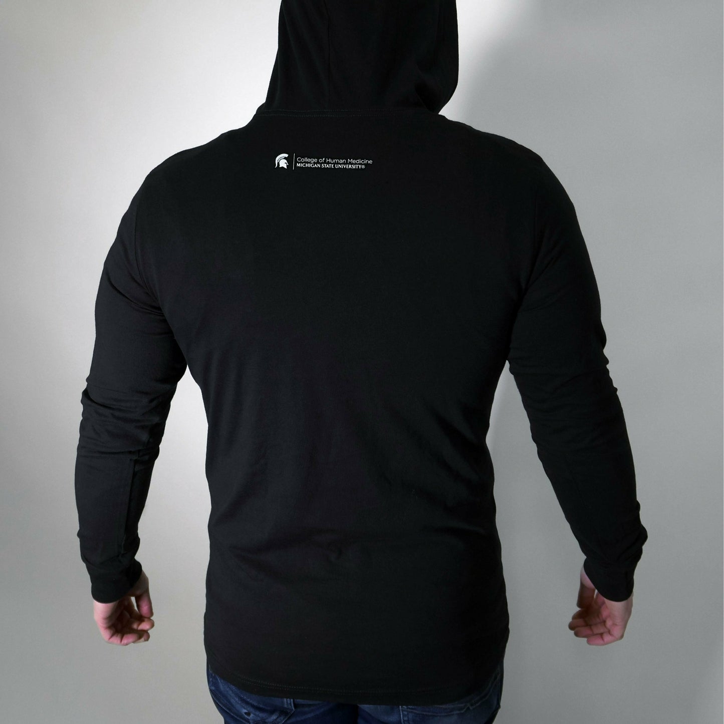 Back of a man wearing the black long-sleeve T-shirt with the hood up. Under the hood is the College of Human Medicine signature logo.