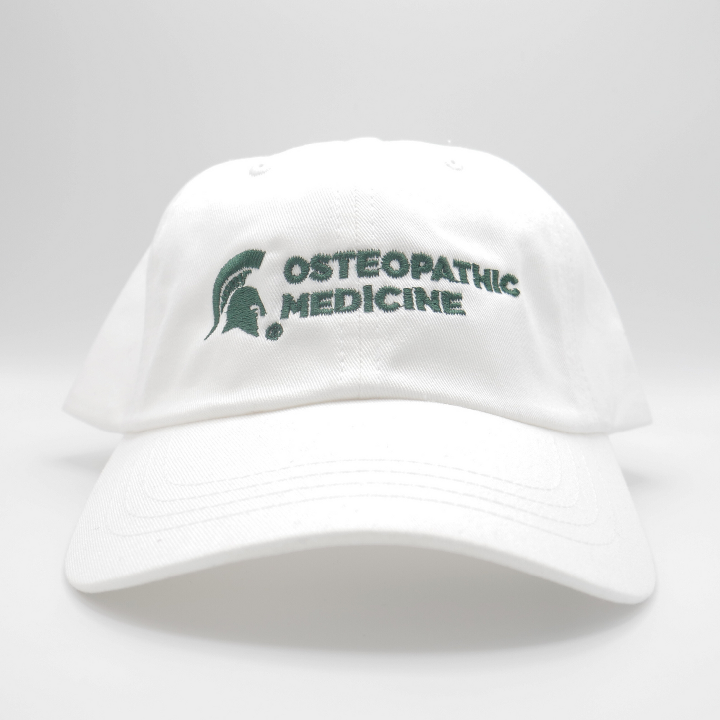 A white ball-cap style hat with a green MSU Spartan Helmet logo and the words Osteopathic Medicine in green on the front of the hat.