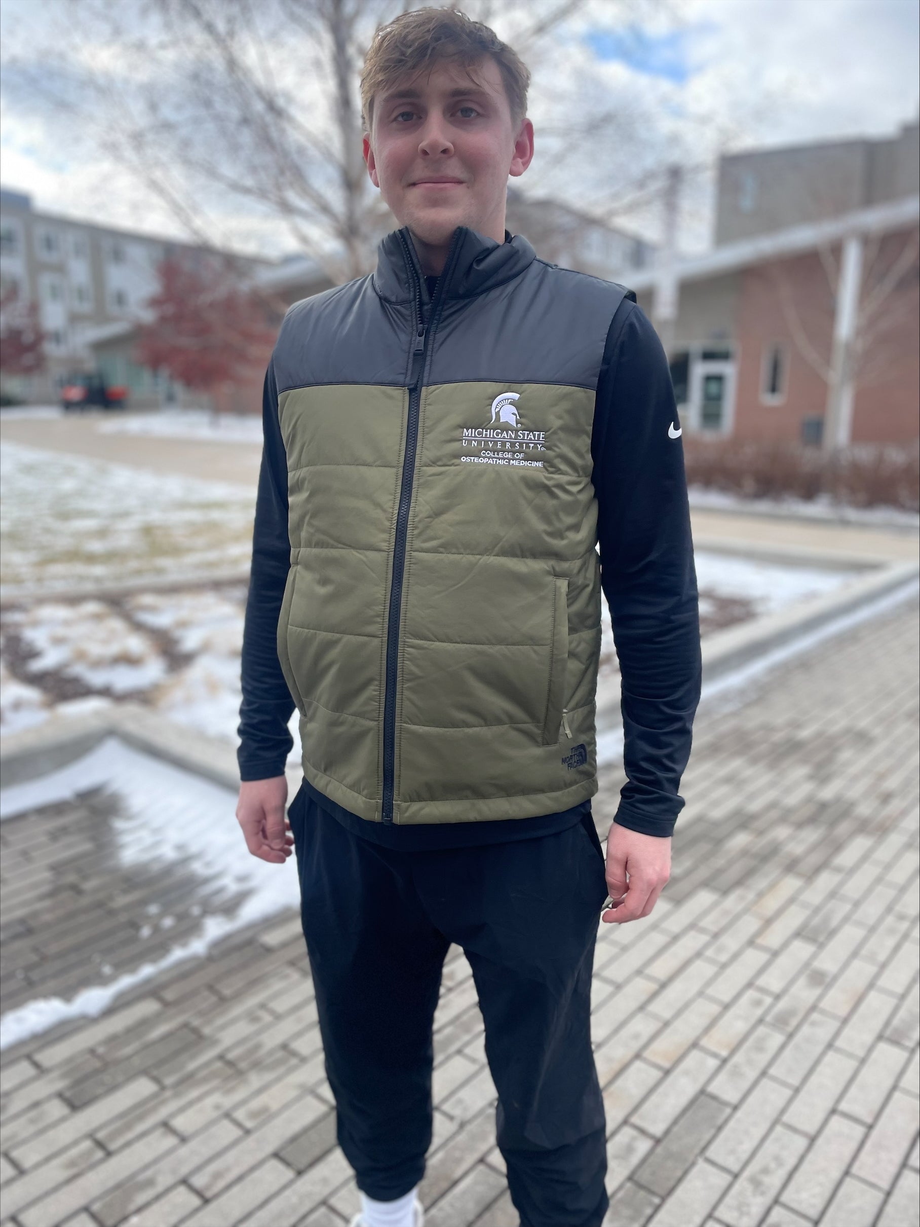 Person wearing a green and black vest with a white embroidered Michigan State University College of Osteopathic Medicine logo on the left chest.