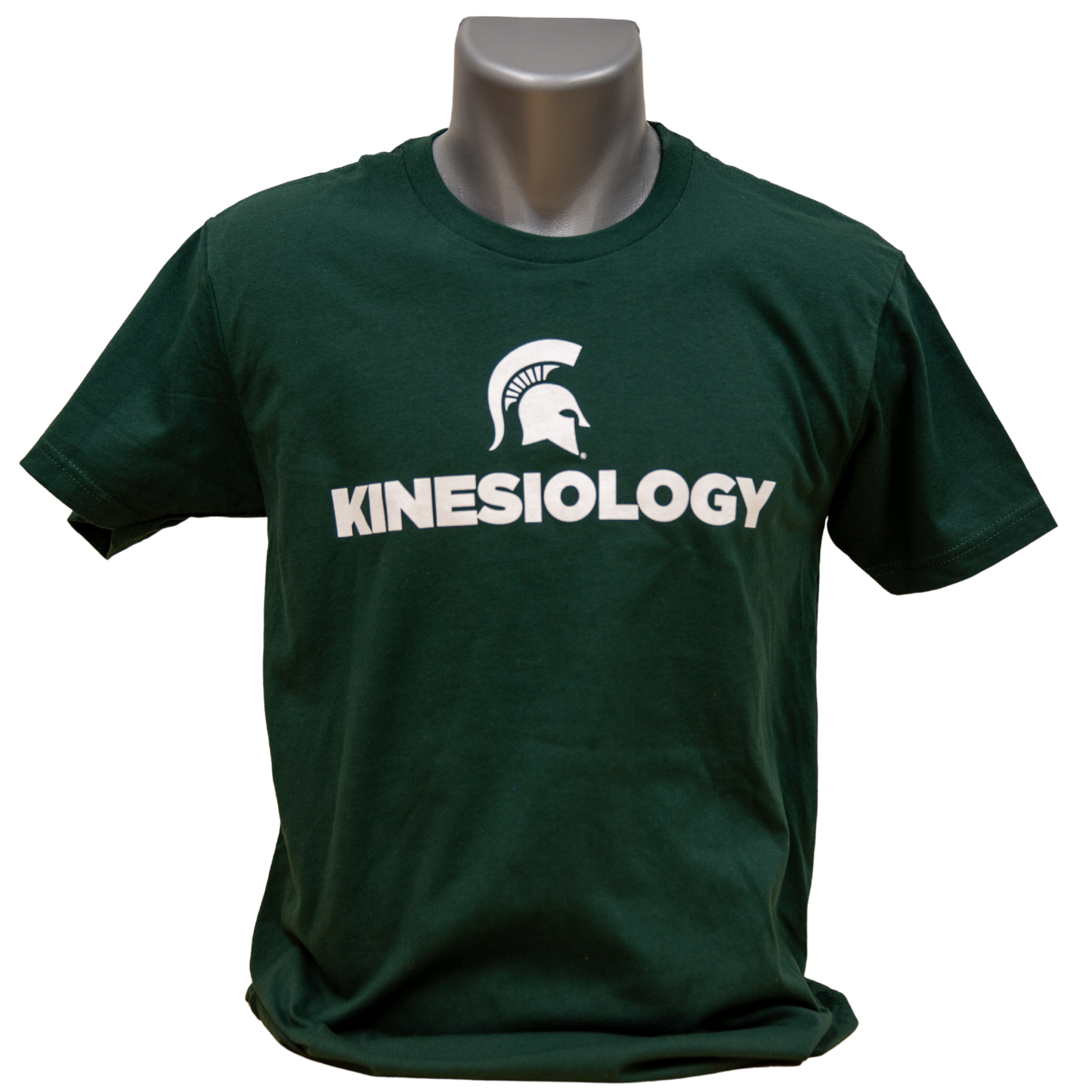 Forest green short-sleeve unisex crewneck T-shirt with a white Spartan Helmet logo above text reading "Kinesiology" in all caps. Shown on a mannequin.
