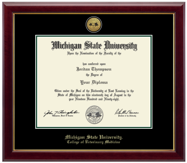 Framed Michigan State University diploma in a dark wood frame with a gold inner edge. The matte is black with a green inner border surrounding the diploma. Michigan State Seal is at the top of matte and is gold engraved. 'Michigan State University' is inscribed in gold at the bottom of the frame. Below Michigan State University is 'College of Veterinary Medicine'.