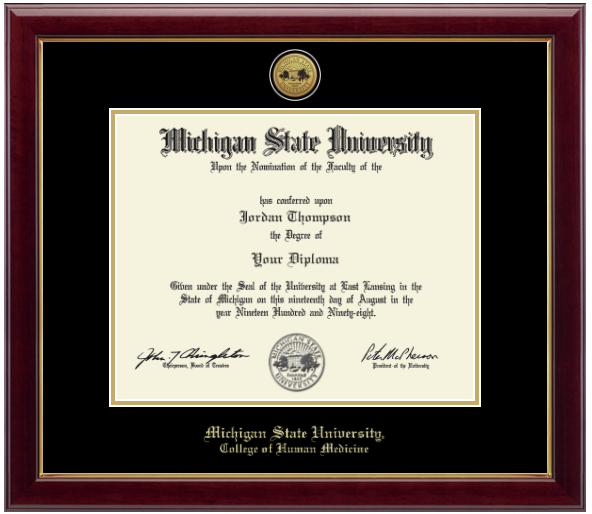 Framed Michigan State University diploma in a dark wood frame with a gold inner edge. The matte is black with a gold inner border surrounding the diploma. Michigan State Seal is at the top of matte and is gold engraved. 'Michigan State University' is inscribed in gold at the bottom of the frame. Below Michigan State University is 'College of Human Medicine'.