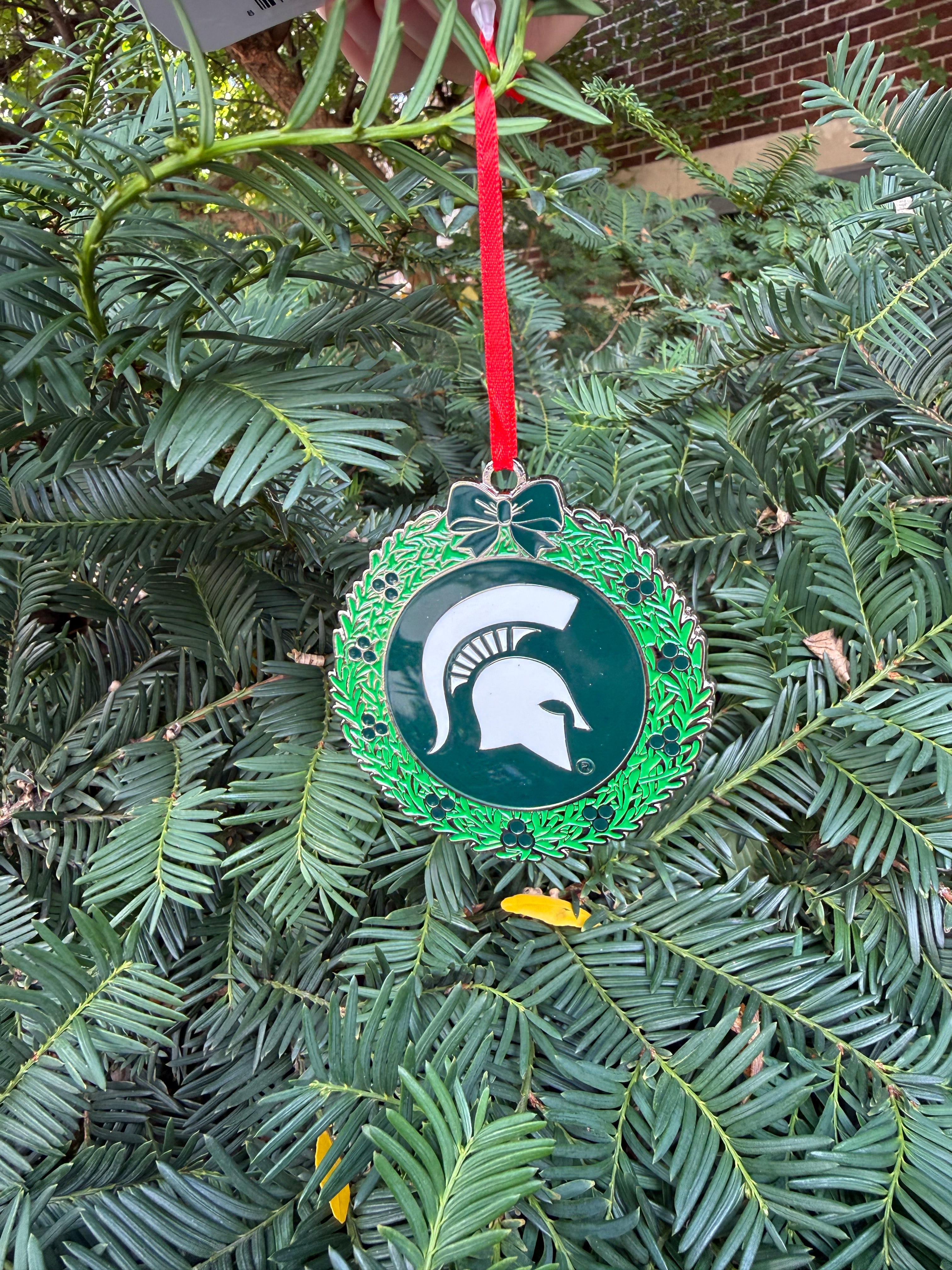 Michigan State themed wreath ornament. The outside of the ornament is decorated as a wreath design and the inside is green with a white Spartan helmet logo in the center.
