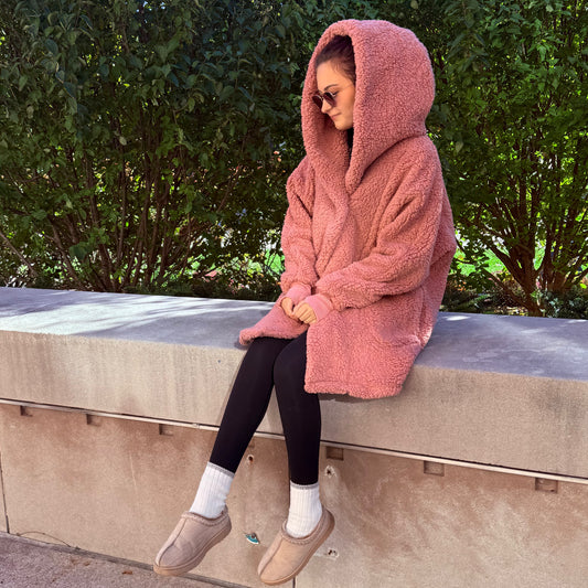Woman sitting outdoors, wearing a long pink lounger with a hood.
