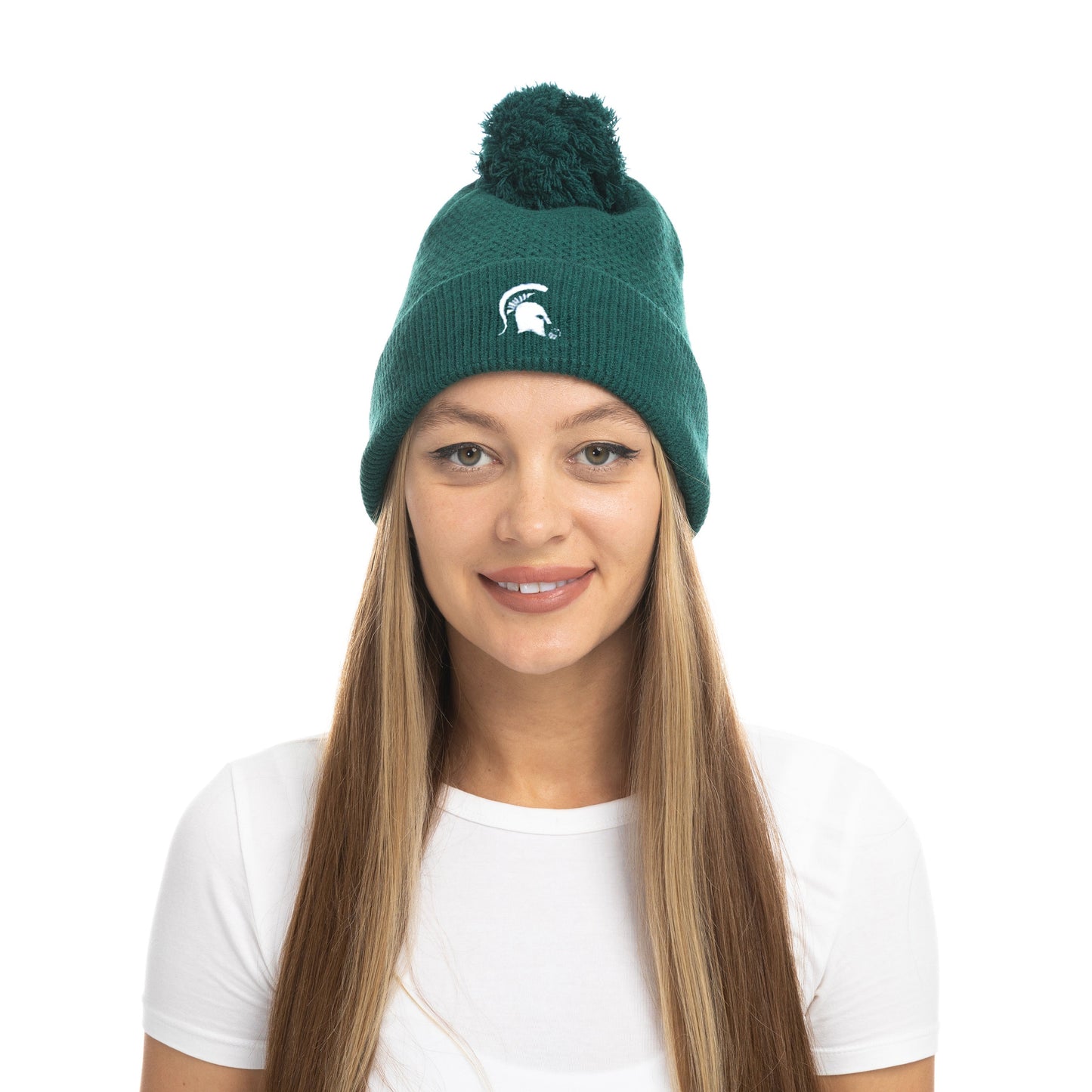 Model wearing a dark green knit beanie with pom-pom and Spartan Helmet logo on the front.