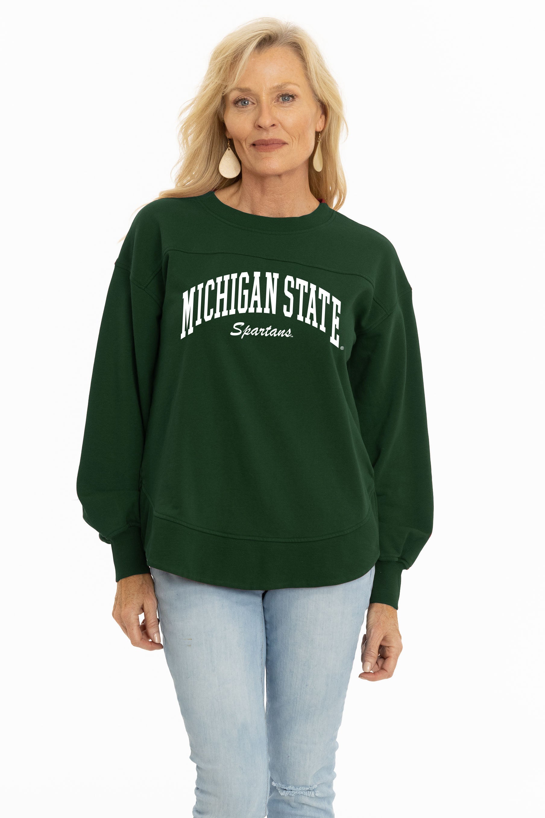 A person wearing a green crewneck sweatshirt with "Michigan State" in block letters and "Spartans" in script. The sweatshirt has balloon sleeves and cuffs at the wrists.