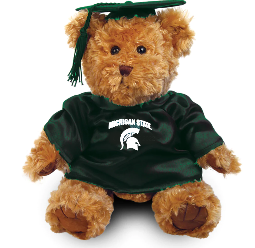 Graduation-themed teddy bear wearing a green shirt with "Michigan State" screen printed text and a Spartan Helmet logo, both in white. On the bear's head is a green graduation cap. Shown on a white background.
