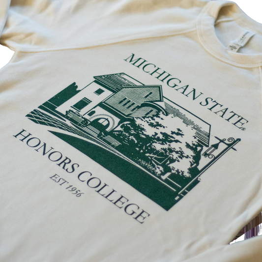 Close up of a natural/tan colored crewneck sweatshirt. On the torso of the sweatshirt in green is an image of the first MSU honors college building. Around the image is the text "Michigan State Honors College est. 1956."