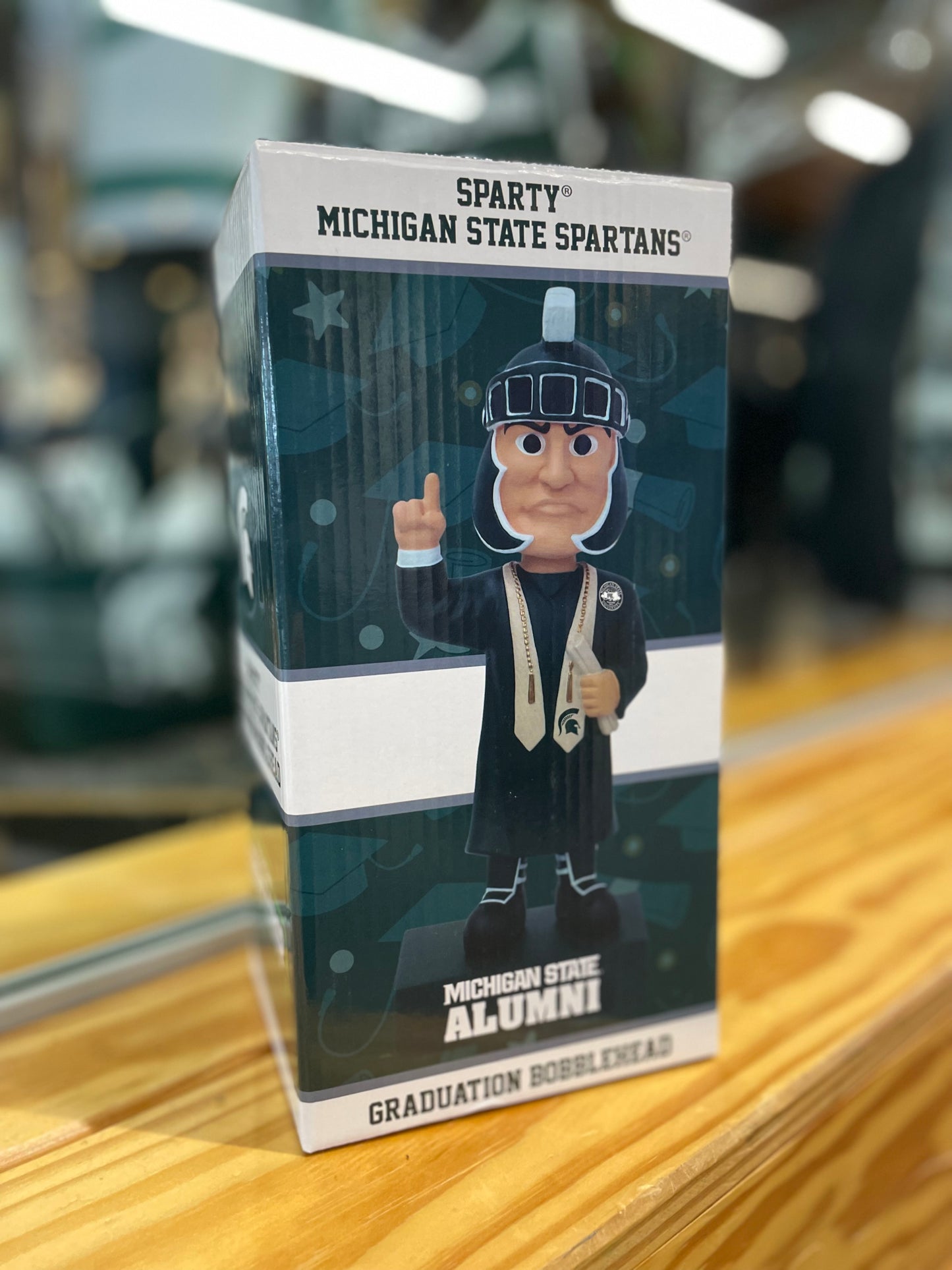 Box image of a graduation Sparty bobblehead wearing graduation attire and featuring bold text that reads "Michigan State Alumni" base.
