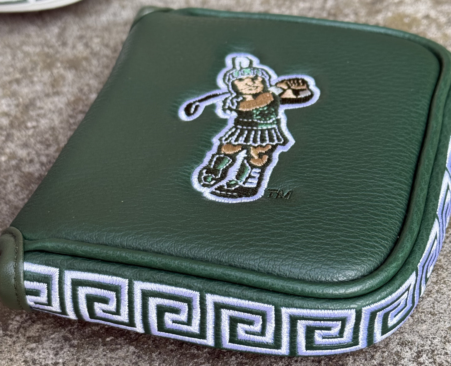 Close up of a green mallet putter headcover with an embroidered Golf Sparty logo on the front and a green and white Greek design on the side.