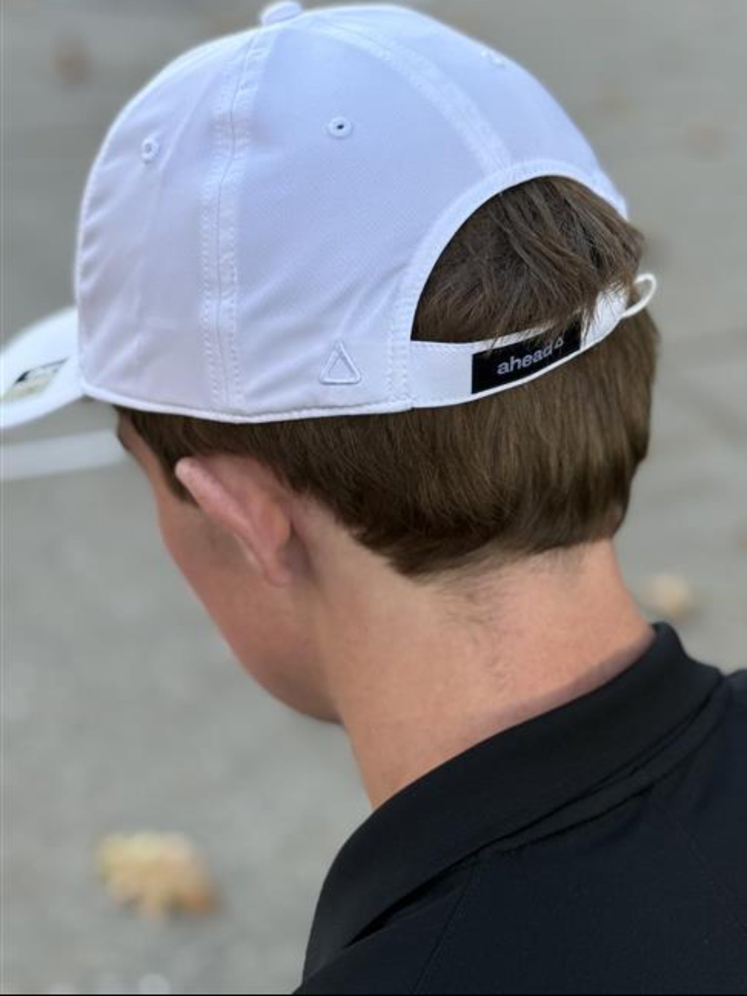 Person wearing a white cap with a brand logo on the back, displaying opening of the back of cap.