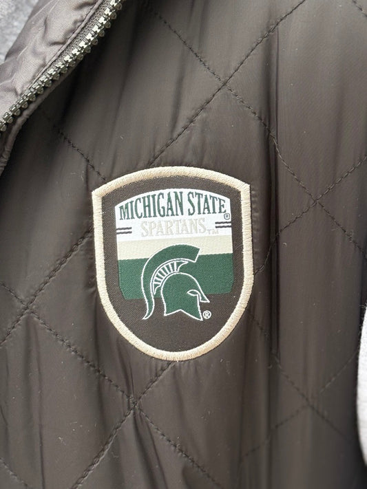 Close up of the a black quilted vest, showing the an official Spartans logo patch on the upper left chest.