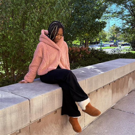 Woman sitting outdoors, wearing a cropped pink lounger with a hood.