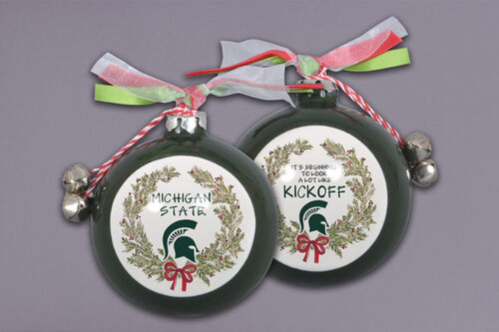 Two green Michigan State University Christmas ornaments with wreath designs, red bows, and Spartan helmet logos. One reads 'MICHIGAN STATE' and the other 'IT'S BEGINNING TO LOOK A LOT LIKE KICKOFF,' both decorated with red, white, and green ribbons and silver bells.