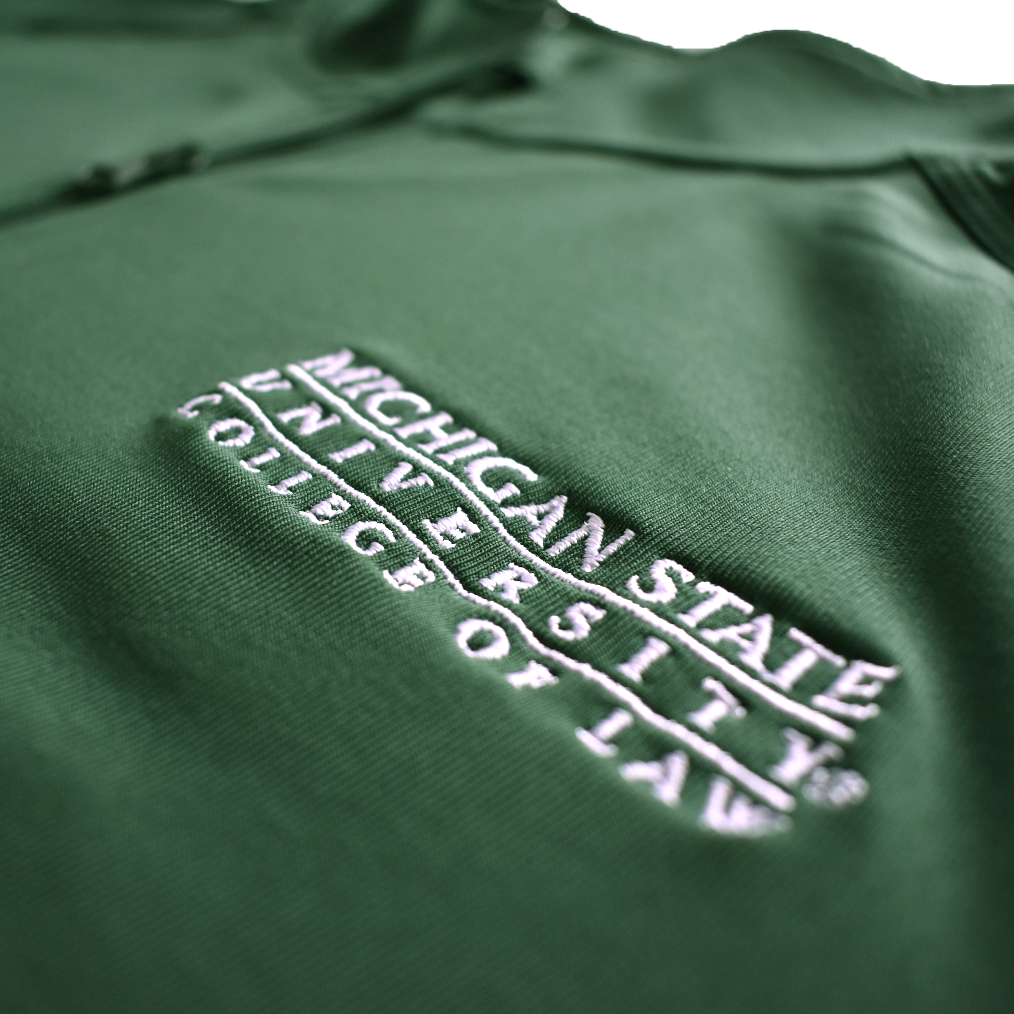 Close-up of the embroidered white Michigan State University College of Law wordmark logo on the left chest of a dark kelly green jacket.