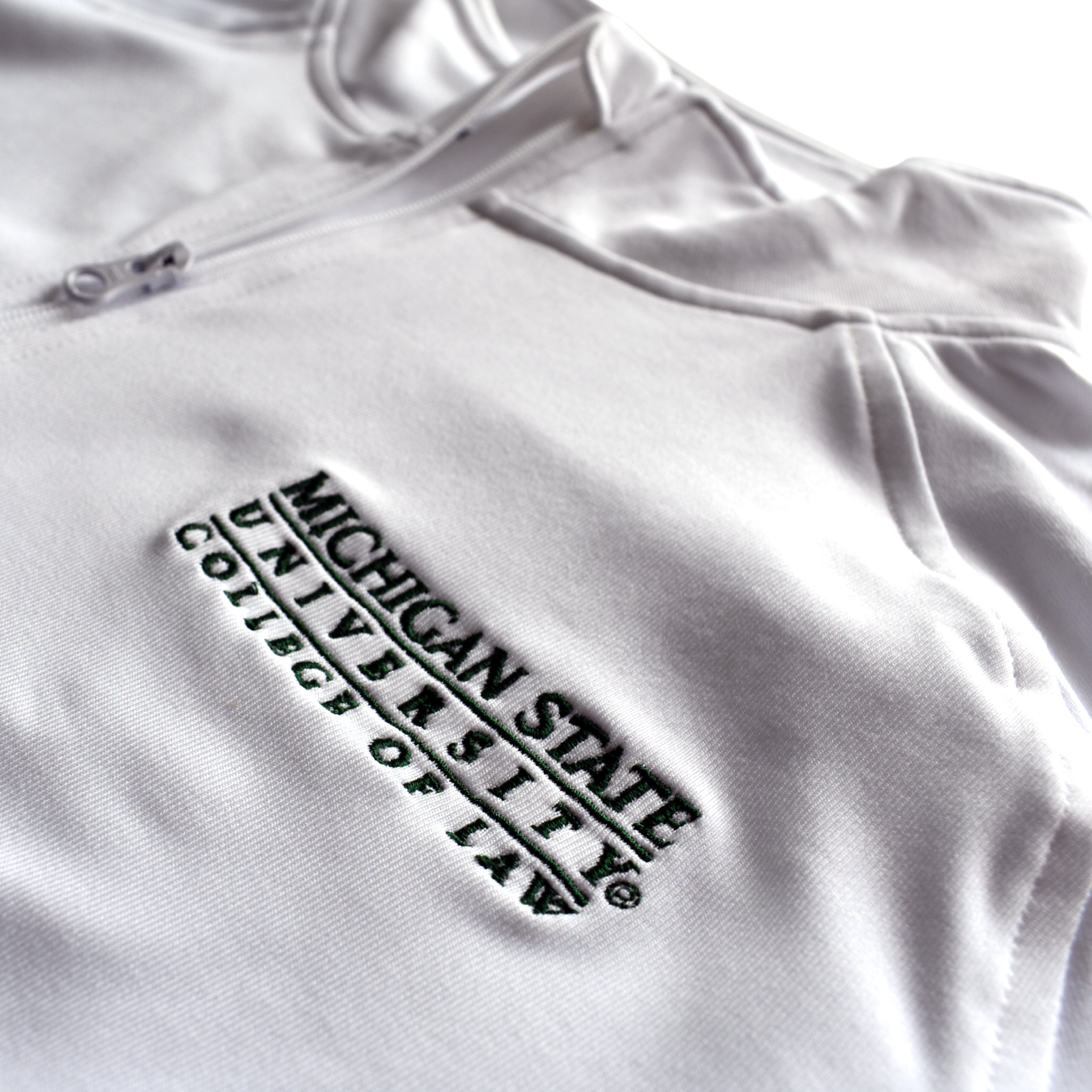 Close-up of the embroidered forest green Michigan State University College of Law wordmark logo on the left chest of a white jacket.