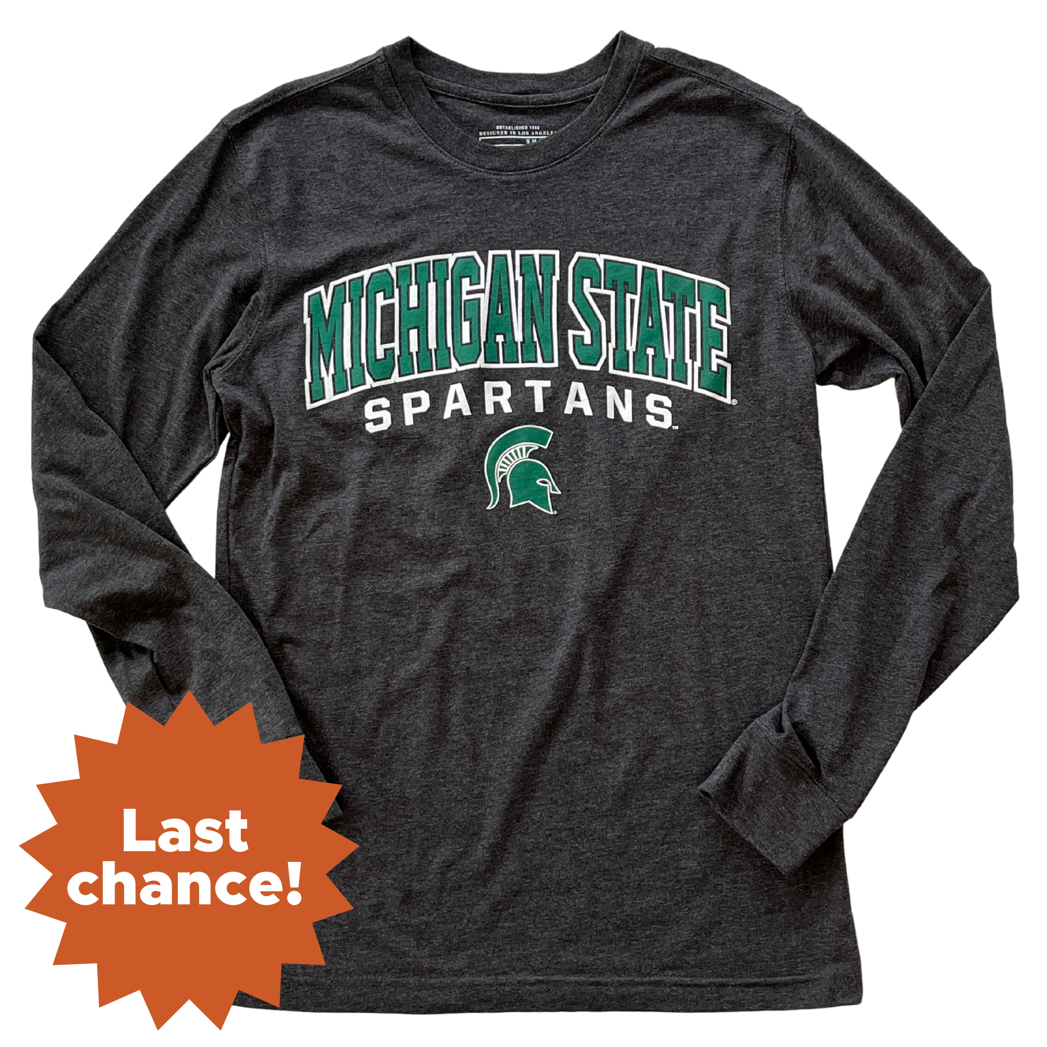 Charcoal long-sleeve t-shirt with green and white printing on the center chest. The two lines of text are slightly curved over a small green Spartan helmet with a white outline. The top line reads Michigan State in green block letters with a white outline, and the bottom line reads Spartans in white block letters. In the lower left corner is an orange sunburst with the words "Last chance!"