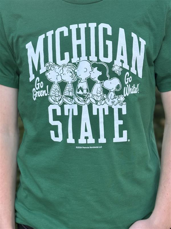 Close up of a green screen printed Michigan State University T-shirt featuring white text that reads 'Michigan State' with 'Go Green!' and 'Go White!' on each side. Below the text are Peanuts characters, including Charlie Brown, Snoopy, and friends.