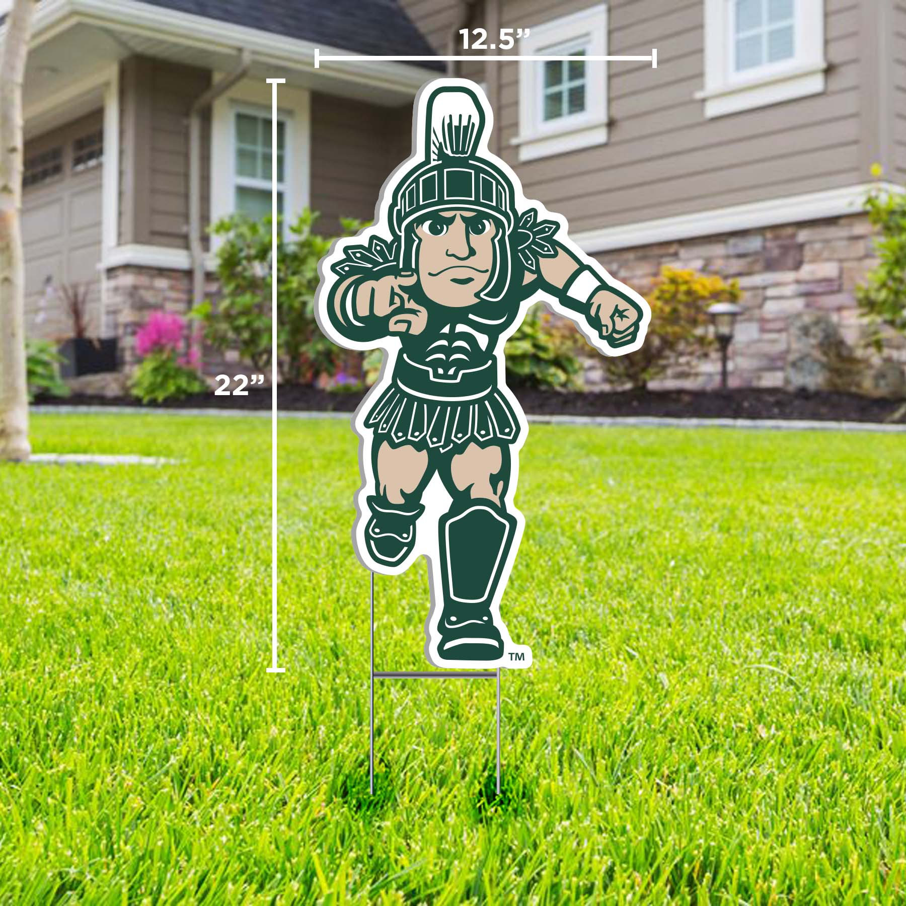 A lawn sign the Running Sparty mascot in green, representing Michigan State University, displayed on a lawn in front of a house.