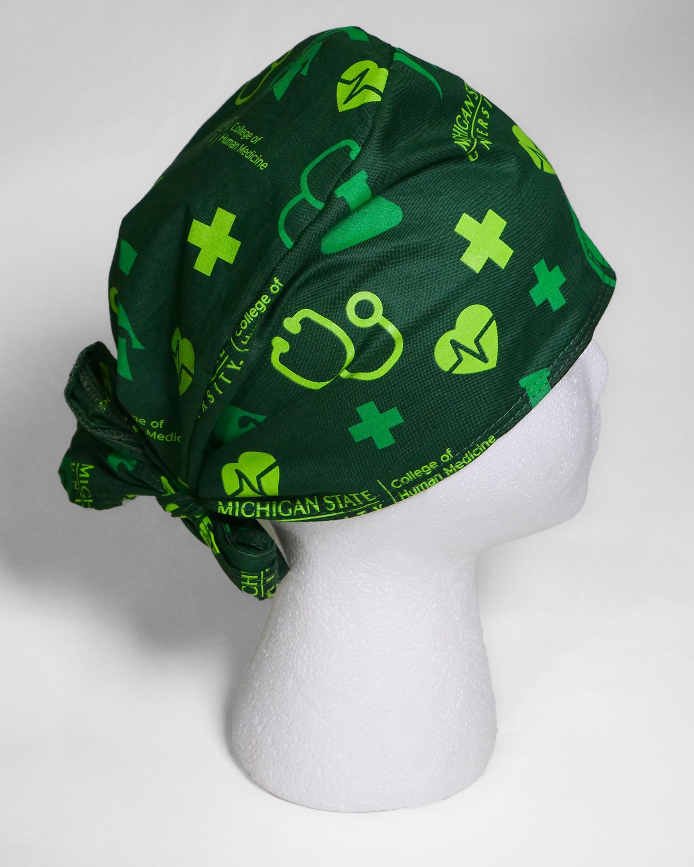 Forest green scrub cap on foam display head. Features lime green and kelly green medical icons printed all over.