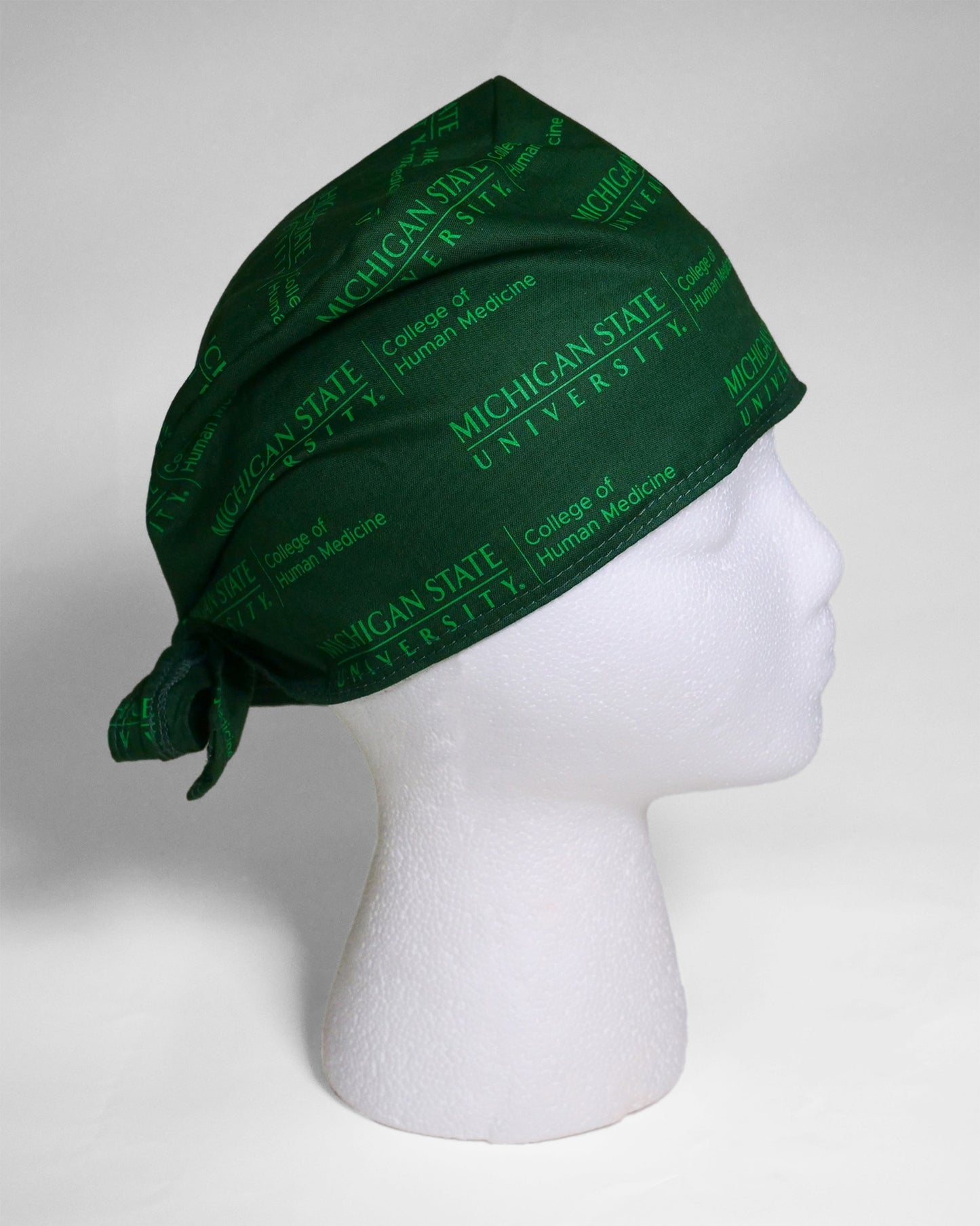Tonal forest green scrub cap with the green Michigan State University College of Human Medicine logo patterned around the cap.
