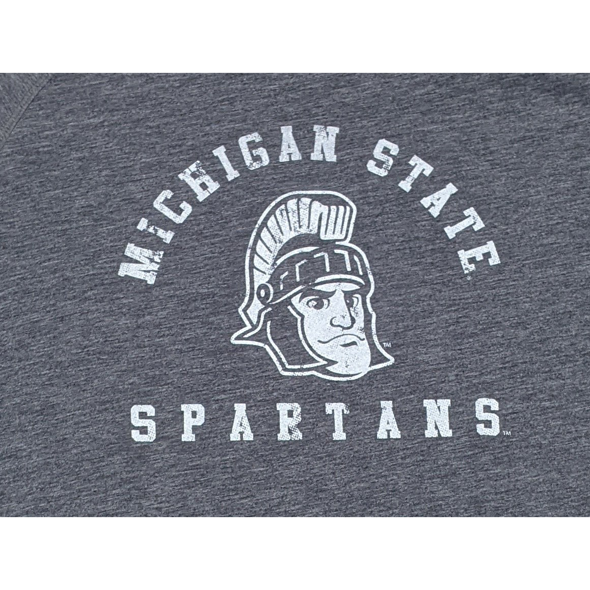 Close-up of a white screen printed rendition of Sparty's head is printed between arched text reading Michigan State and a straight line of text reading Spartans.