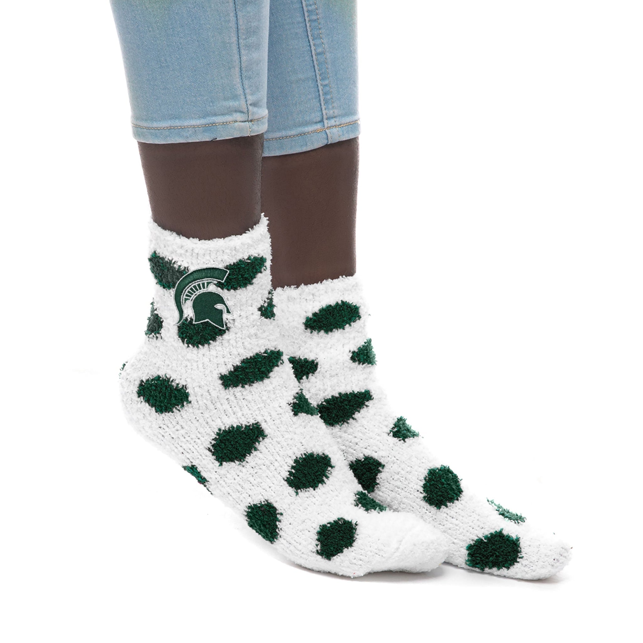 Feet wearing fuzzy white socks with large green polka dots and a Michigan State Spartan helmet logo near the ankle.