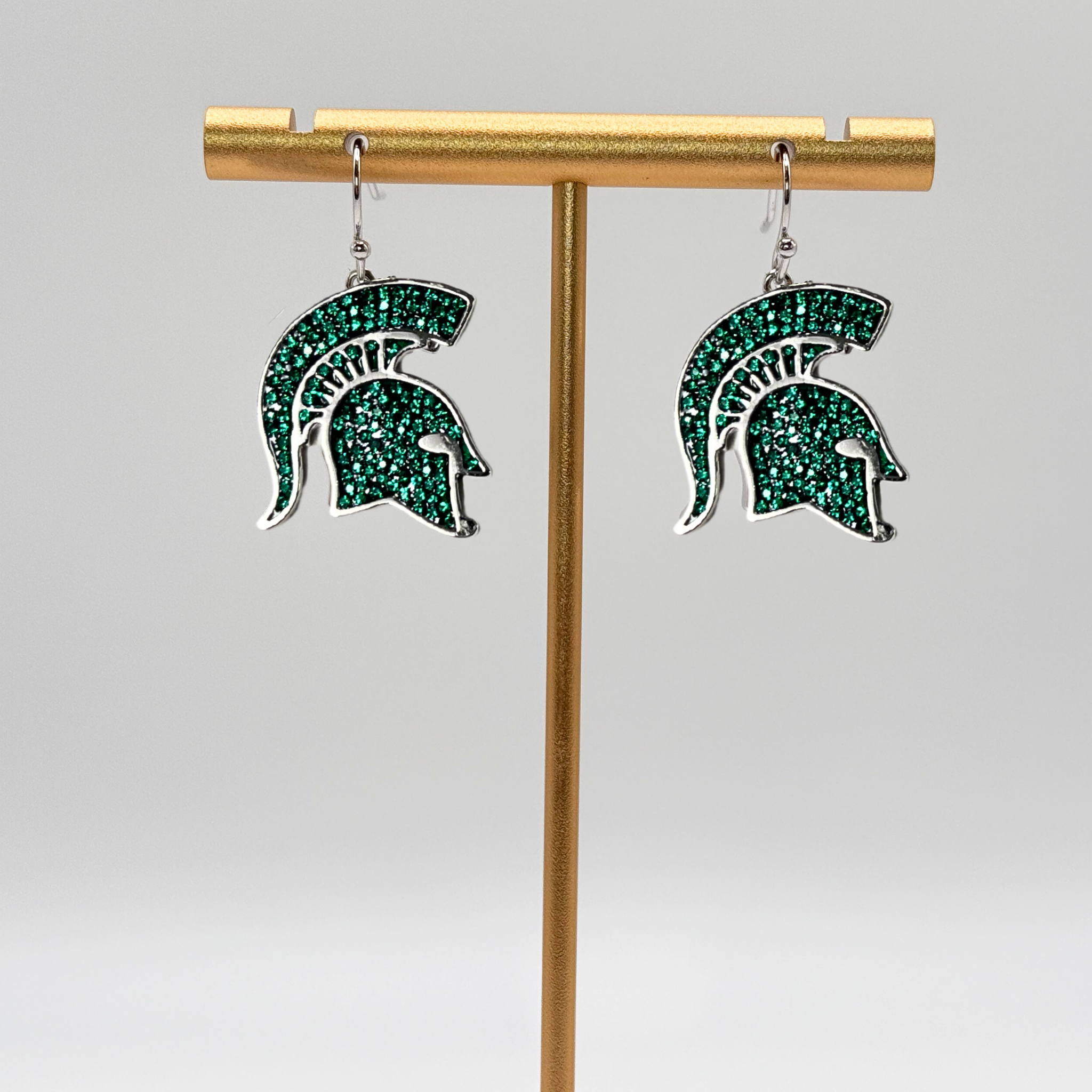 A pair of dangle earrings shaped as the Michigan State Spartan helmet logo. The logo is comprised of small green crystals with a rhodium plated brass outline.