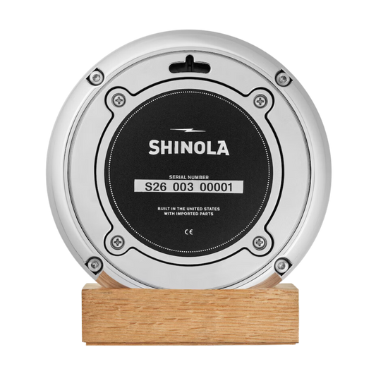 Shinola desk clock case back on a wooden stand.