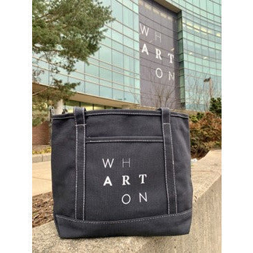 A black cotton and canvas tote bag. On the side of the bag spells the word Wharton in a staggered formation.