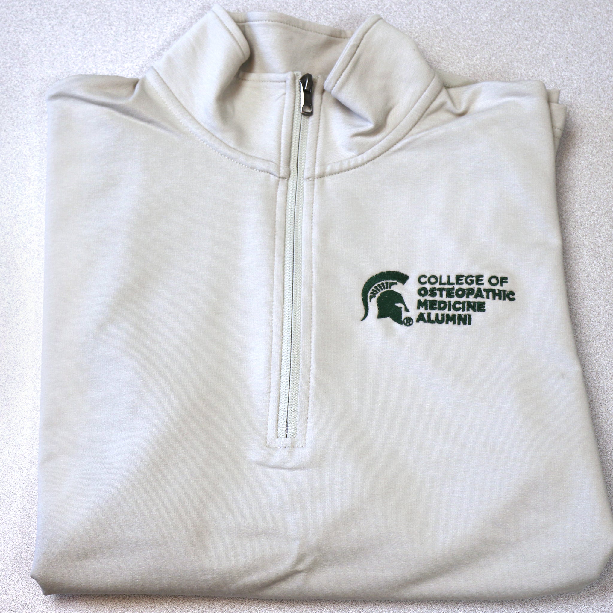 Front of cream quarter-zip pullover with College of Osteopathic Medicine logo embroidered in forest green on the left front upper chest.