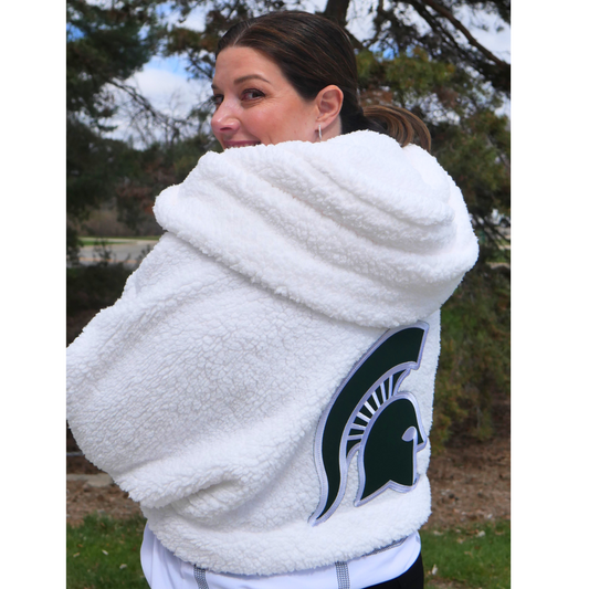 Back of person wearing a cropped white fleece lounger with hood with large green Spartan Helmet logo patch on the center. Hits at waist.
