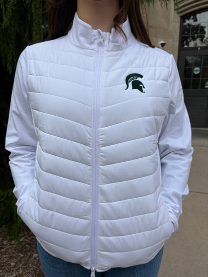 Close up of a woman standing outside, wearing a white two-way zip jacket with puff stitching on the middle section and a green Spartan Helmet on the left chest. 