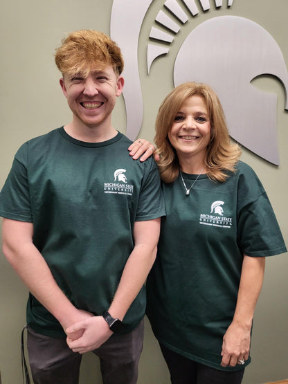 Two people with green T-shirts, featuring the Veterinary Medical Center logo and Spartan Helmet in white on the left upper chest.