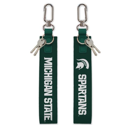 Front and back of a dark green MSU themed key strap. On the left side of the image is the front of the key strap with silver hardware and white text that reads "Michigan State." On the right side of the image is the back of the key strap with silver hardware and the Spartan Helmet logo in white followed by white text that reads "Spartans."
