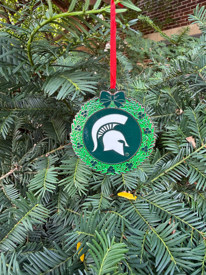 Close up of Michigan State themed wreath ornament. The outside of the ornament is decorated as a wreath design and the inside is green with a white Spartan Helmet logo in the center. 