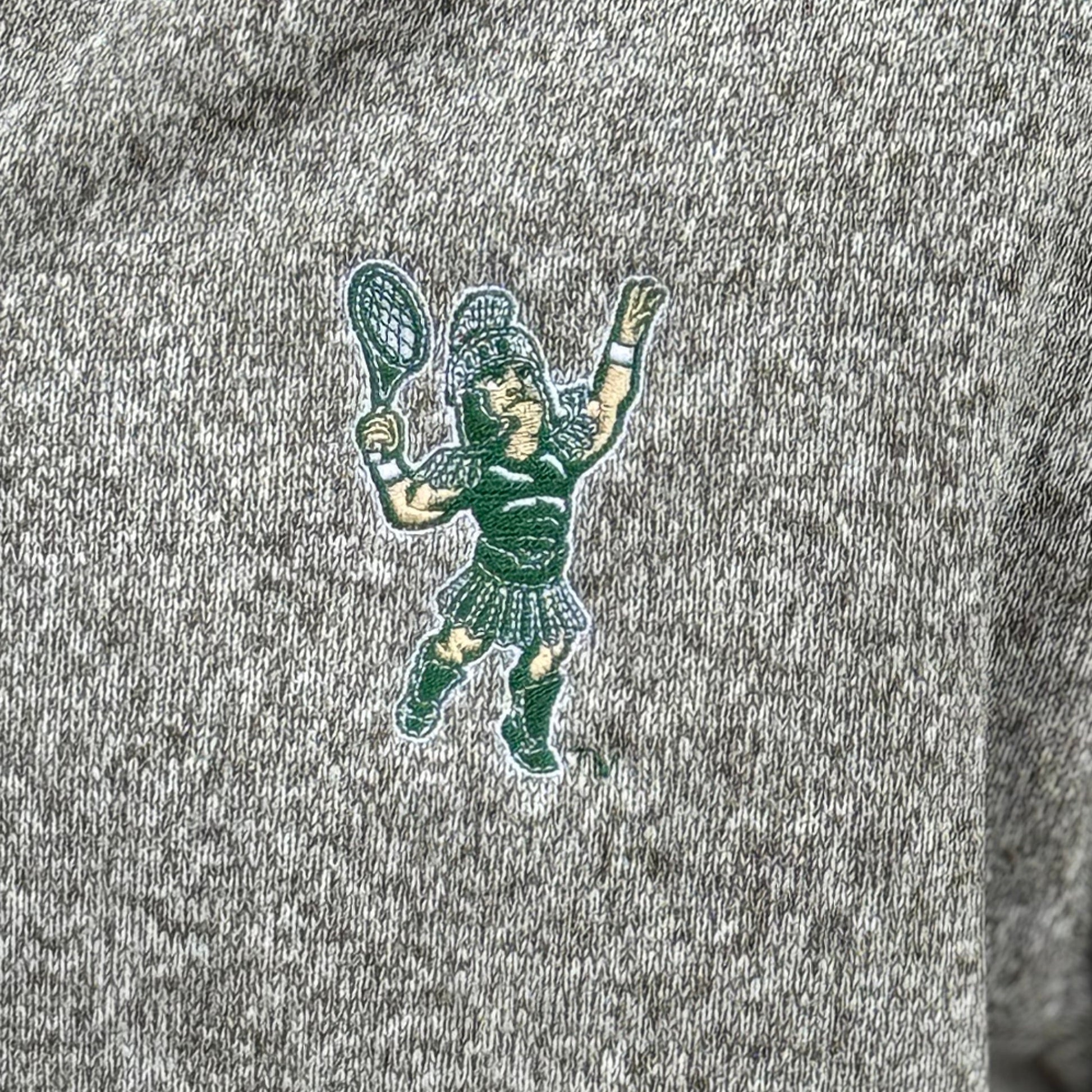 Close up of the embroidered Sparty playing tennis on the upper left chest of the full zip jacket.