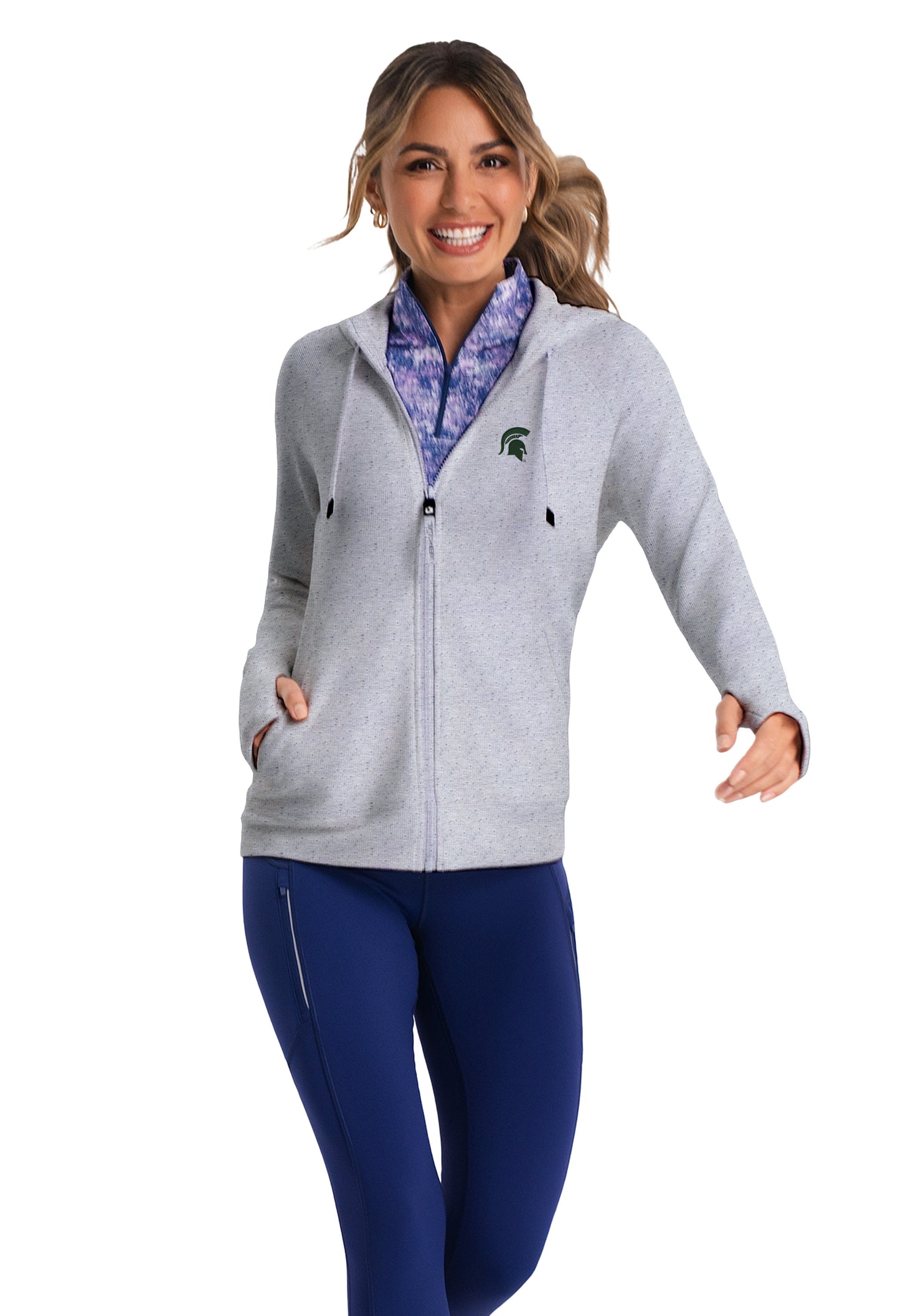 Woman wearing a light gray full-zip jacket with a drawstring hood, a pocket on either side, thumb holes at the end of the sleeves, and a green Spartan Helmet logo on the upper left chest. 