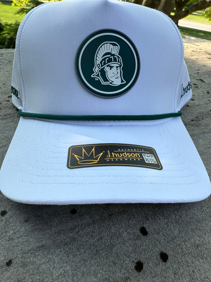 White cap leaning on concrete outside featuring a Gruff Sparty design on the front with a green cord above the brim.