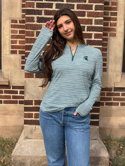 Woman standing outdoors, wearing a green and white striped quarter-zip pullover with a green Spartan Helmet logo on the left upper chest. 