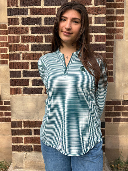 Closer angle of a woman standing outdoors, wearing a green and white striped quarter-zip pullover with a green Spartan Helmet logo on the left upper chest. 