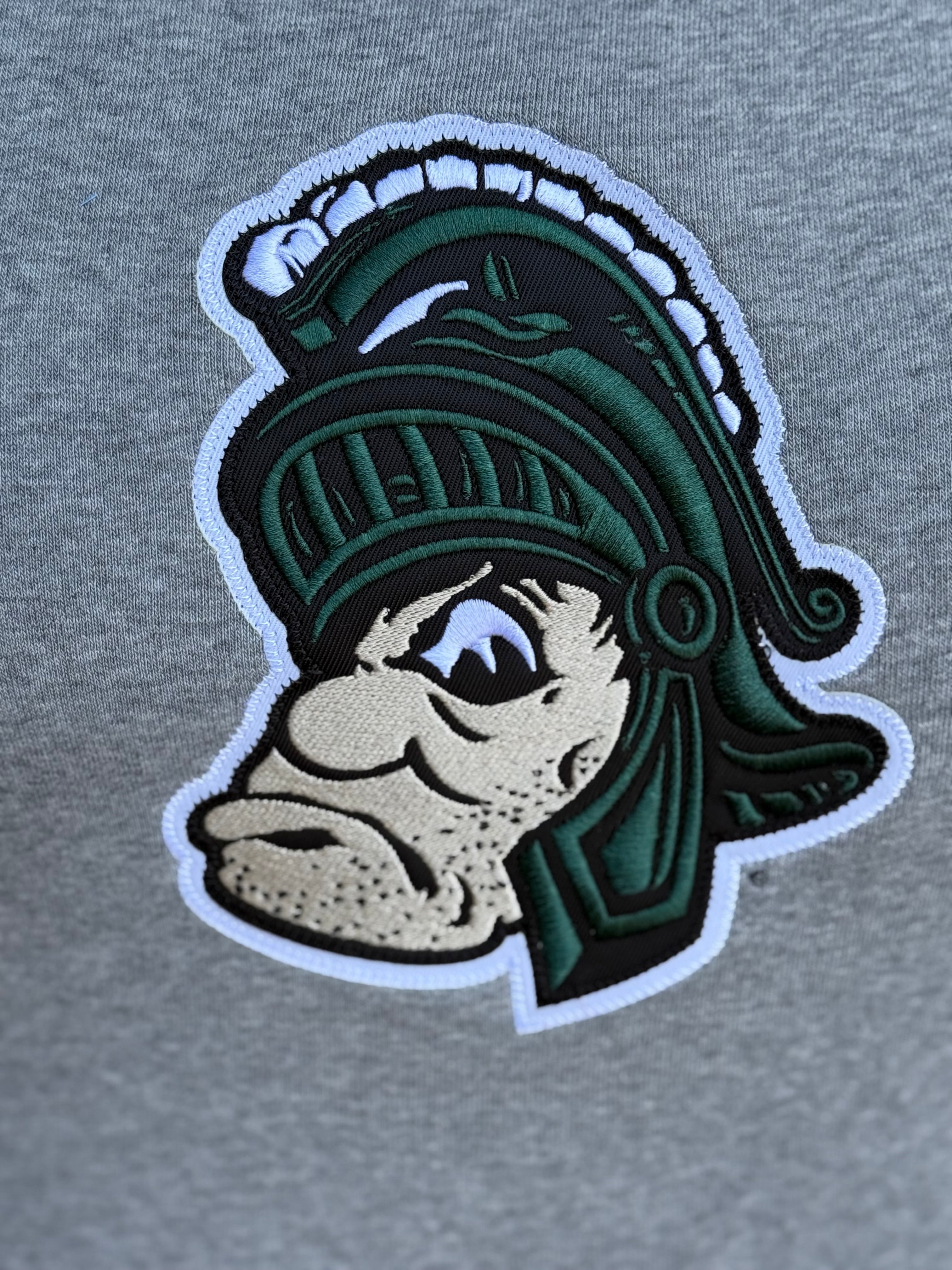 Close up of a gray crewneck, showing the embroidered Gruff Sparty logo. 