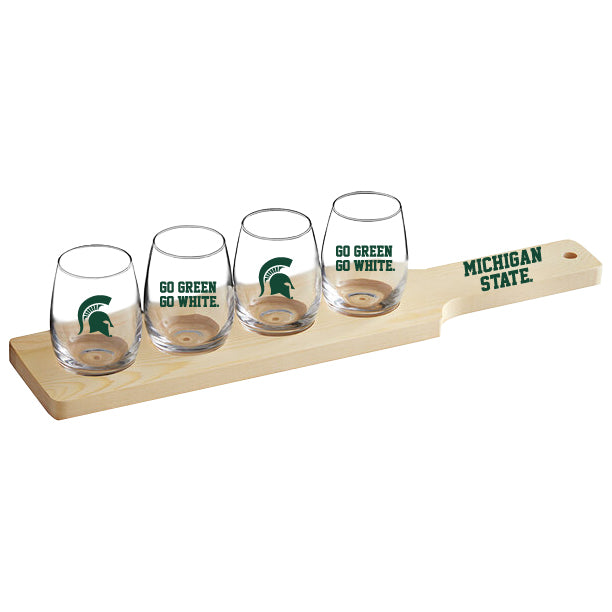 Michigan State Spartans four-piece stemless glass tasting set displayed on a natural wood serving flight board. The clear glasses feature green Spartan helmet logos and “GO GREEN GO WHITE” graphics, while the wooden paddle is printed with “MICHIGAN STATE” in green.