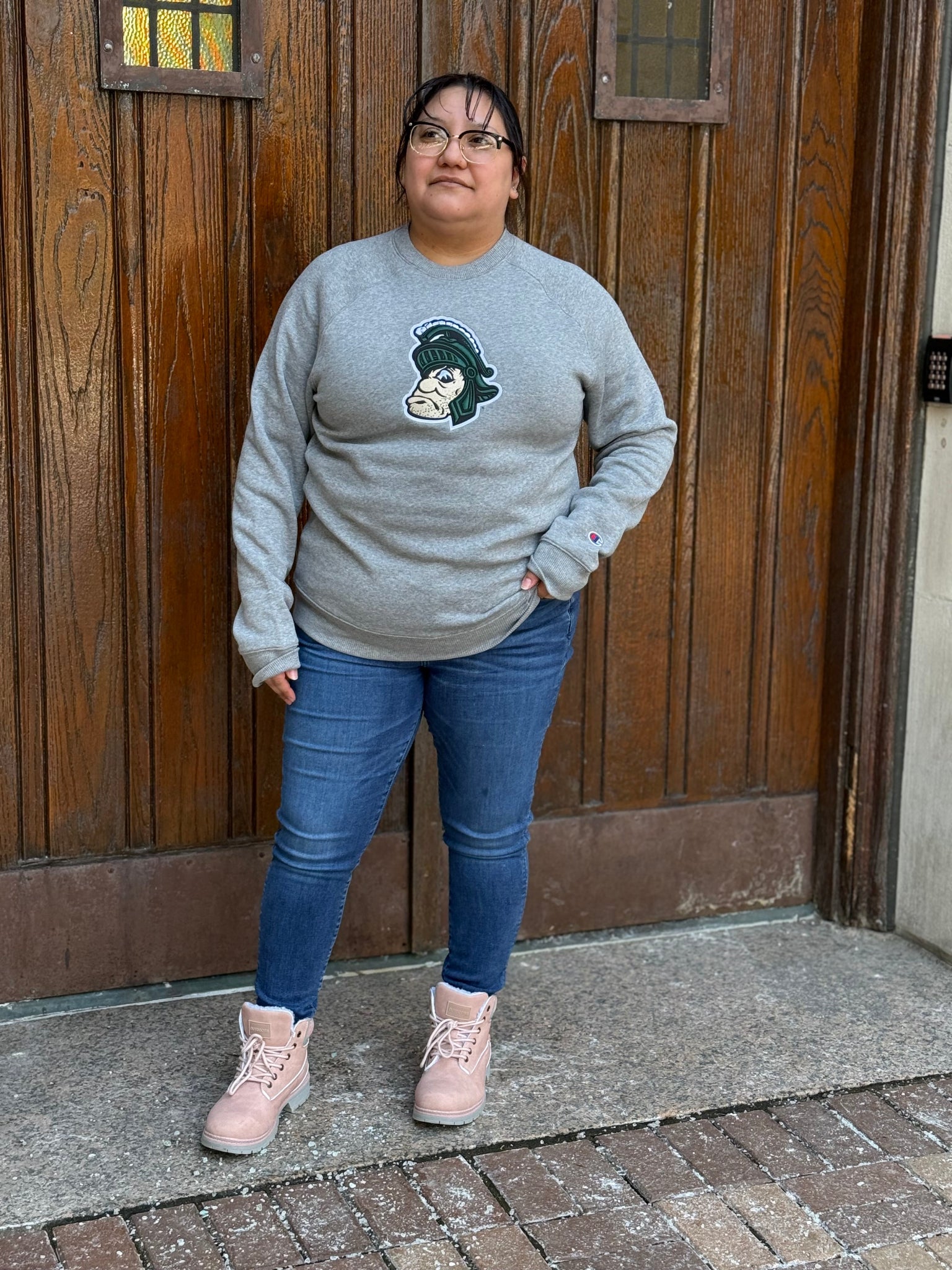 Woman wearing a gray crewneck with the Gruff Sparty logo embroidered on the front chest. 