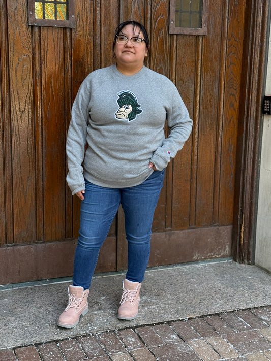 Woman wearing a gray crewneck with the Gruff Sparty logo embroidered on the front chest. 